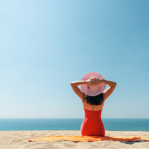 Beautiful woman sitting on the golden beach with hat