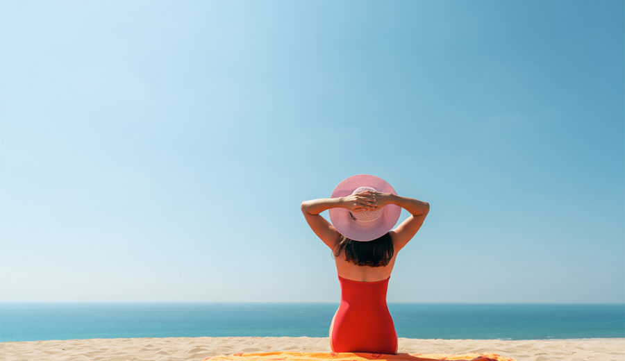 Beautiful woman sitting on the golden beach with hat