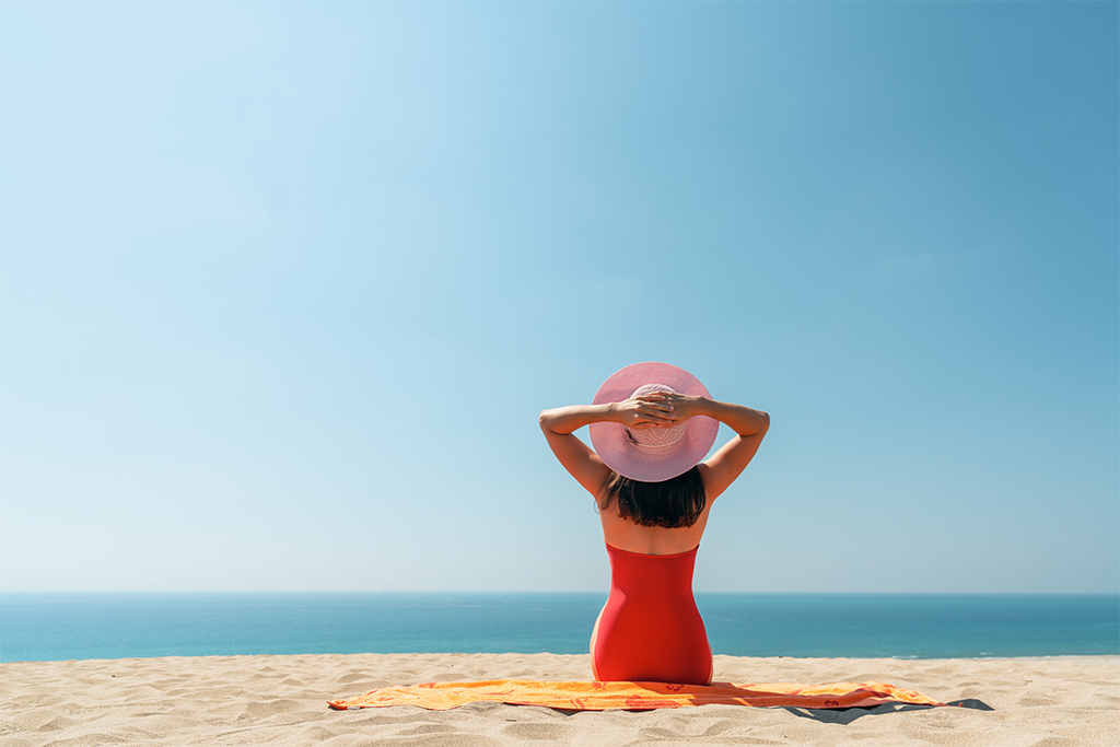 Beautiful woman sitting on the golden beach with hat