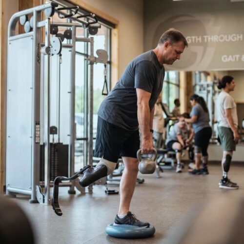 Person with lower limb prosthetic performing adaptive strength training exercises in a gym setting